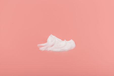White beauty cream lotion highlighter smear swatch smudge on pink peach background