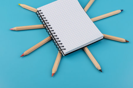 multicolor pencils and blank notebook on blue background with copy space
