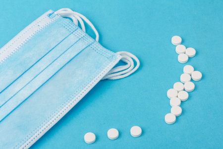 Prevent virus. Medical protective mask with white pills, isolated on blue background. Disposable...