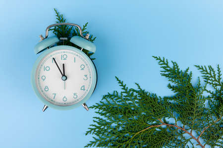 Winter holiday background with blue alarm clock and cypress branches on blue background.の写真素材