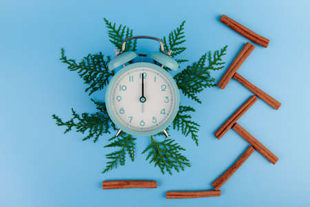 Blue alarm clock and green cypress branch on blue background. Christmas composition, copy space.の写真素材