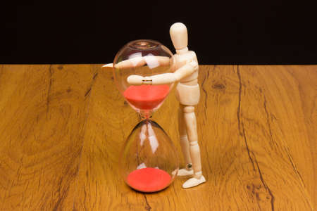 The wooden mannequin next towards the hourglass. keeping timeの写真素材