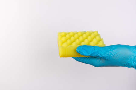 Female hand in blue gloves for cleaning and cleaning products for home holds a yellow sponge on an isolated white backgroundの写真素材
