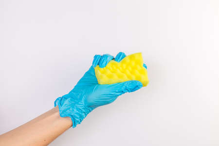 Female hand in blue gloves for cleaning and cleaning products for home holds a yellow sponge on an isolated white backgroundの写真素材