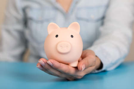 Piggy bank in hands on blue background, space for text. Finance, saving moneyの写真素材