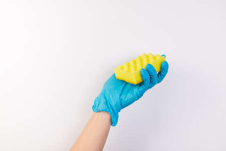 Female hand in blue gloves for cleaning and cleaning products for home holds a yellow sponge on an isolated white backgroundの写真素材
