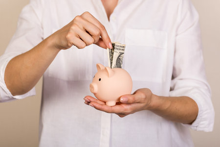 pink piggy bank with money (usa one Dollar banknotes). human hand putting money in piggy bank....