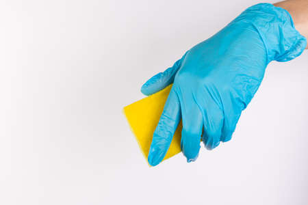 Female hand in blue gloves for cleaning and cleaning products for home holds a yellow sponge on an isolated white backgroundの写真素材