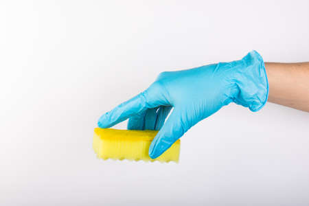 Female hand in blue gloves for cleaning and cleaning products for home holds a yellow sponge on an isolated white backgroundの写真素材