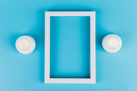 White jar of skin cream and white photo frame on blue background. Place for text. Copy spaceの写真素材