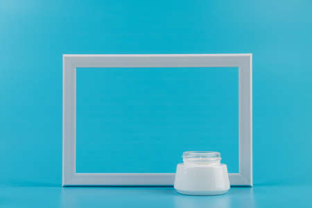 White jar of skin cream and white photo frame on blue background. Place for text. Copy spaceの写真素材