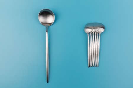 Clean empty big table spoon and small spoons on blue background, top view. Dining and kitchenware conceptの写真素材