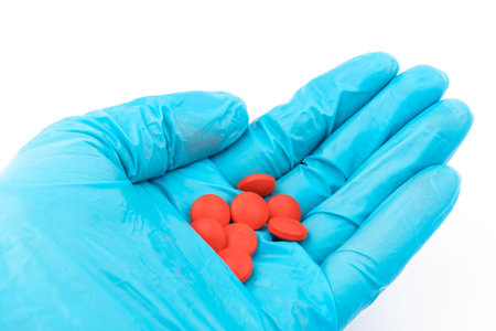 Gloved hands with red pills, The hand of the medical worker in medical gloves holding pills