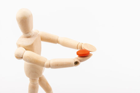 Wooden ball-jointed doll holding a pill in front of its face. Concept of medicine and healthの写真素材