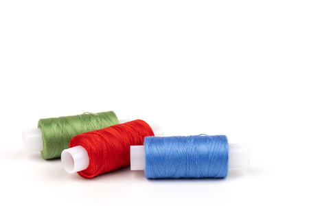 Sewing threads of different colors on reels on white background. Free space, close-up.