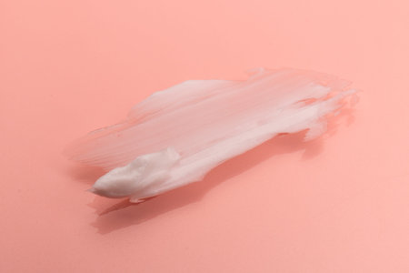 White smear of cosmetic cream isolated on pink background. Creamy foundation texture. Smear of face...