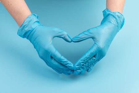 Person in latex gloves showing heart gesture against light blue background, closeup on handsの写真素材