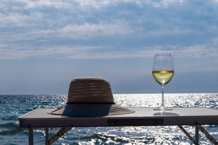 A glass of white wine. Wine against the backdrop of the sea coast and a sunny summer beach. Wine tasting and relaxation at the resortの写真素材