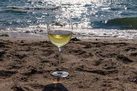 A glass of white wine. Wine against the backdrop of the sea coast and a sunny summer beach. Wine tasting and relaxation at the resortの写真素材