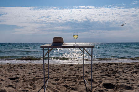 A glass of white wine. Wine against the backdrop of the sea coast and a sunny summer beach. Wine tasting and relaxation at the resortの写真素材