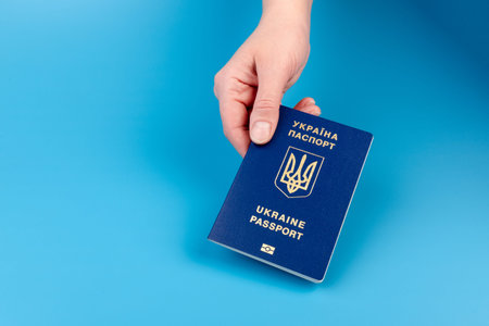 Human hand with Ukrainian international biometric passport closeup on blue background. Document used for travel outside Ukraine.の写真素材