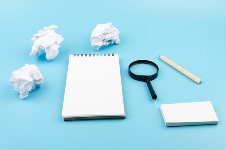 Paper balls, magnifying glass and color pencils over blank white sheet of note book - Creativity...