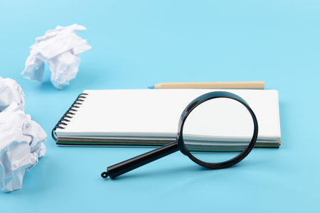 Paper balls, magnifying glass and pencil over blank white sheet on blue - Creativity crisis concept.の写真素材