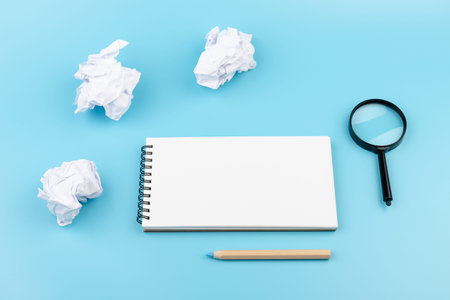 Paper balls, magnifying glass and color pencils over blank white sheet of note book - Creativity...