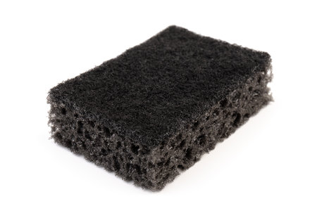 Black sponge used for washing dishes isolated on white. Has two surfaces which are rough and smooth.の写真素材
