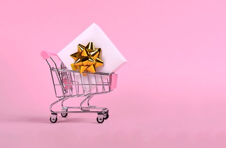 White gift box with bow in shopping cart isolated on pinkの写真素材