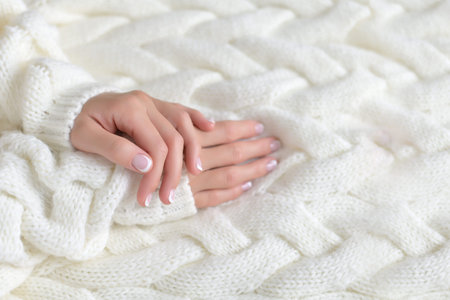 Womens beautiful hands with French manicure on the background of a white warm sweaterの写真素材