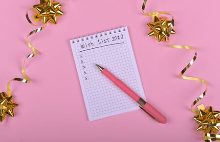 Pen writing in empty notebook decorated with Christmas decorations on the pink background. Top view, flat lay, copy spaceの写真素材
