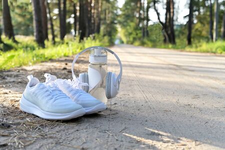 White sneakers, a bottle of water and headphones, a set for running in the woods on a forest road in springの写真素材