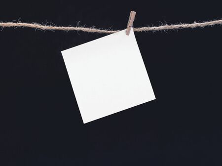 A white square piece of note paper hangs on clothespins on a black background, mock upの写真素材