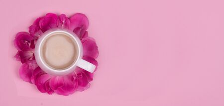 Cup of coffee in rose petals on a pink background, top viewの写真素材