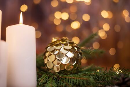 Golden Christmas ball on a tree branch, white candle flame, bokeh lights on a backgroundの写真素材