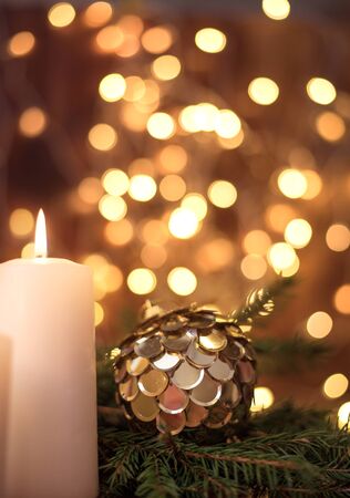 Golden Christmas ball on a tree branch, white candle flame, bokeh lights on a brown backgroundの写真素材