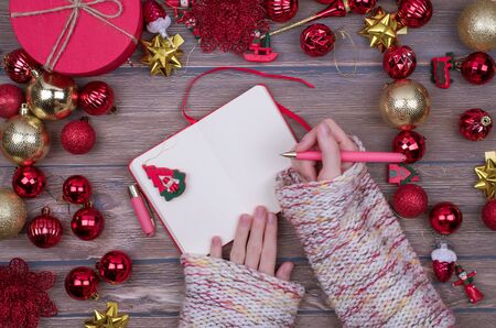 Woman hands write Christmas checklist, letter to Santa on wooden background with christmas ball. Flat lay.の写真素材