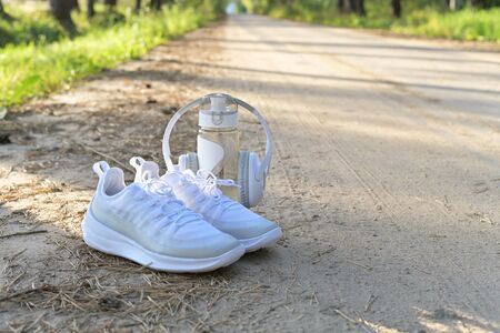 White sneakers, a bottle of water and headphones, a set for running in the woods on a forest road.の写真素材