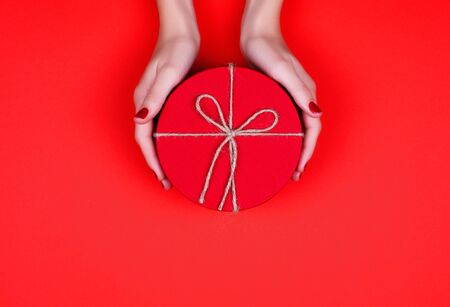 Closed red round gift box on red background. the view from the top. Gift for the holidays of New Year, Christmas, Valentine's day, March 8.の写真素材