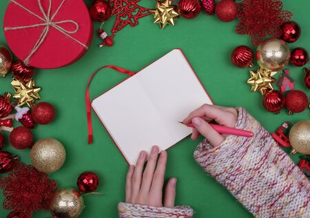 Woman hands write Christmas checklist, letter to Santa, your invitation or advent activities on green background. Top view. Flat lay. copy spaceの写真素材