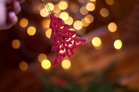 Red decorative Christmas tree branches in woman hand. Bokeh in the background. Christmas card. New Year 2020の写真素材