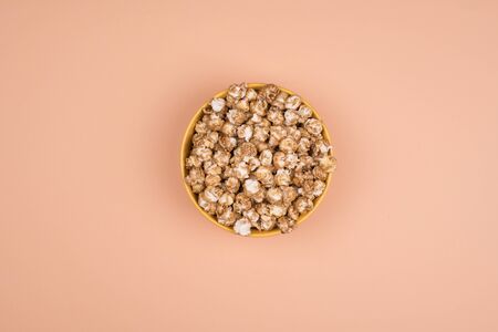 Caramel sweet popcorn bowl isolated on pastel orange background top view. Frame composition with copy space.の写真素材
