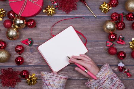 Woman hands write Christmas checklist, letter to Santa, your invitation or advent activities on wooden background. Top view. Flat lay. copy spaceの写真素材