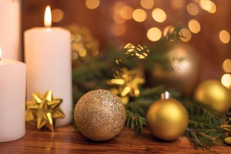 Golden Christmas ball on a tree branch, white candle flame, bokeh lights on a backgroundの写真素材