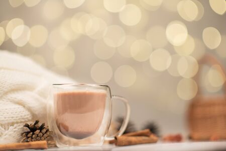 Transparent Cup of warm cocoa on the background of sweaters and evening lights, New Year drink. Christmas drink, winter holiday moodの写真素材