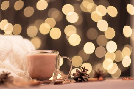 Transparent Cup of warm cocoa on the brown background of sweaters and evening lights, New Year drink. Christmas drink, winter holiday moodの写真素材