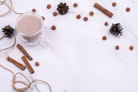 Hot cocoa in a glass cup surrounded by winter things wiyh cinnamon on a white table. The concept of cosy holidays. Flat Layの写真素材