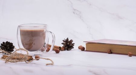 Hot cocoa in a glass cup surrounded by winter things with cinnamon on a white table. The concept of cosy holidays. Flat Layの写真素材