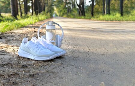 White sneakers, a bottle of water and headphones, a set for running in the woods on a forest road in springの写真素材